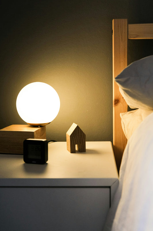 A dark bedside table at night with a small lamp and clock, suggesting a steady, repeatable bedtime routine