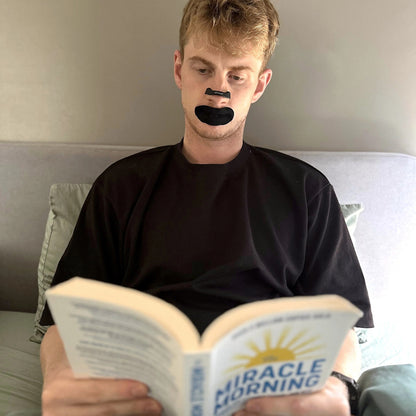 Man reading in bed wearing 18pointthree Mouth Tape