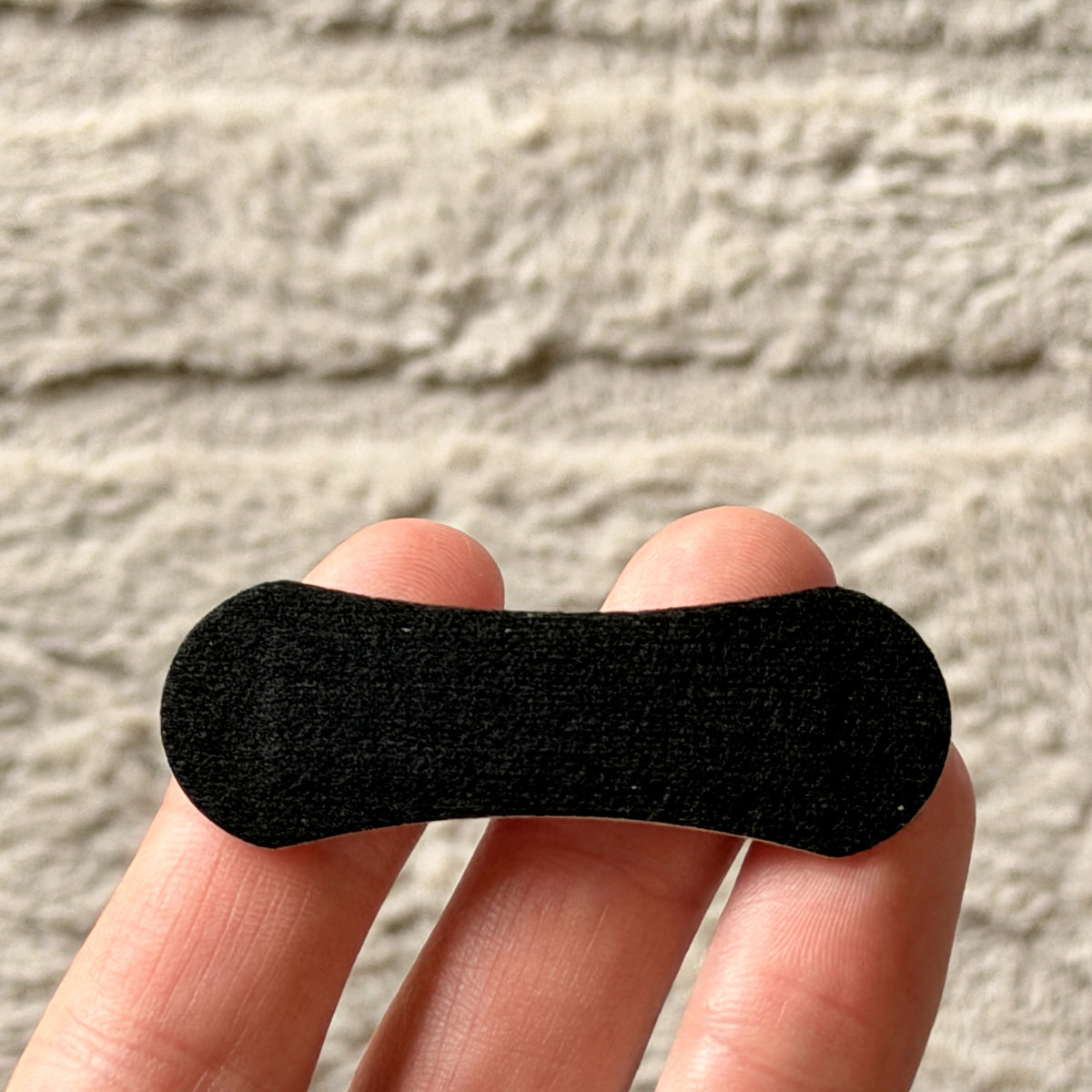 A single nasal strip held across two fingers for scale