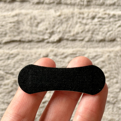 A single nasal strip held across two fingers for scale