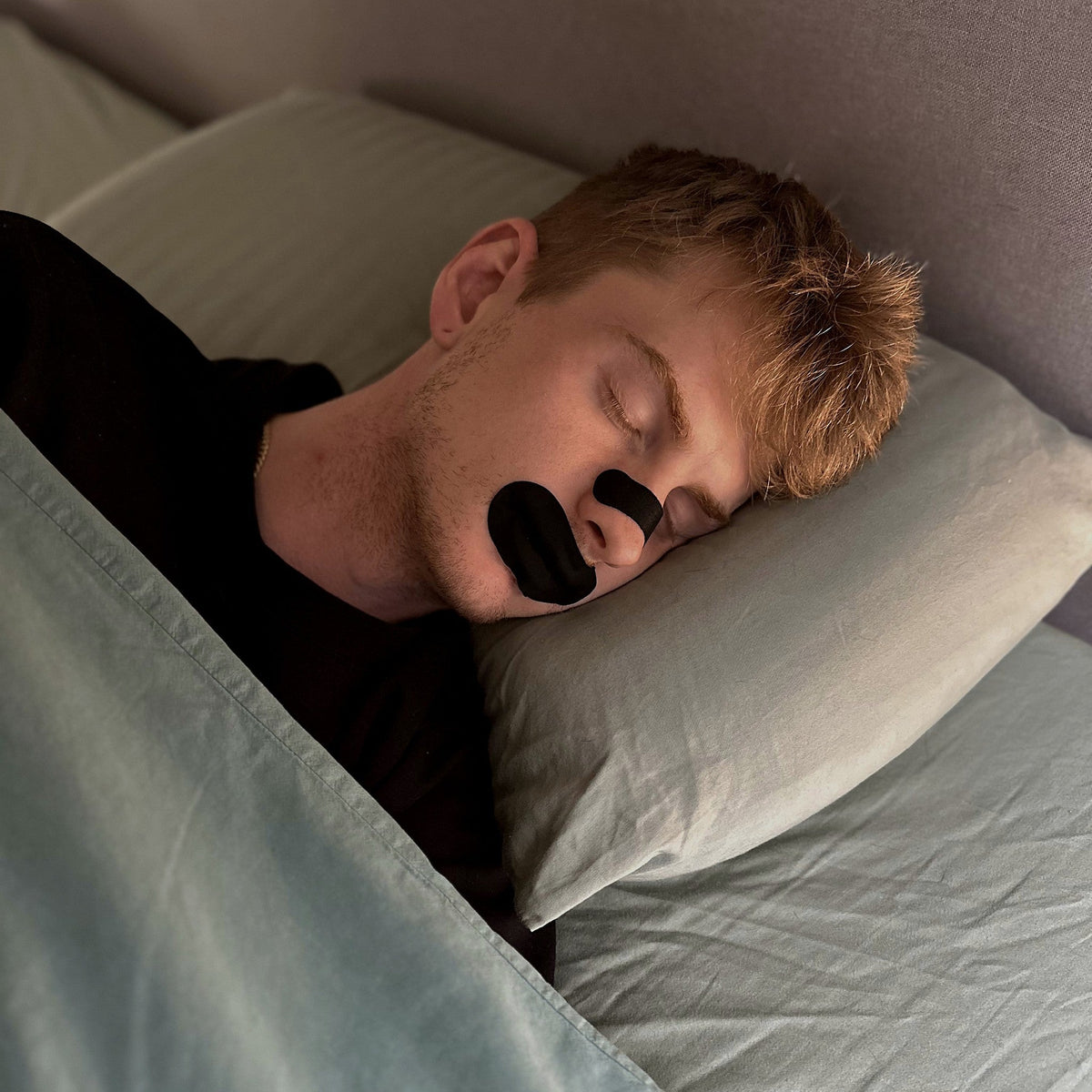 Man asleep wearing an 18pointthree nasal strip and mouth tape
